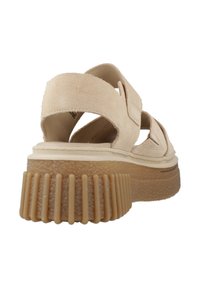 Sandal suede beige dengan tali silang, sol cokelat bercorak, dan desain platform dengan aksen beralur.