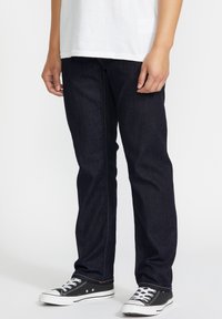 Jeans de mezclilla azul oscuro con corte recto, con costuras naranjas y combinados con zapatillas bajas en blanco y negro.