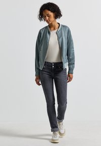Veste bomber bleu clair avec fermeture éclair à l'avant, poignets élastiques et poches latérales, associée à un jean gris foncé ajusté et des baskets blanches.