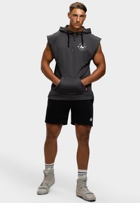 Dunkelgrauer ärmelloser Hoodie mit einer Vordertasche, schwarze Shorts und graue High-Top-Sneaker. Mit einem Logo auf der Brust und einer Kapuze mit Kordelzug.