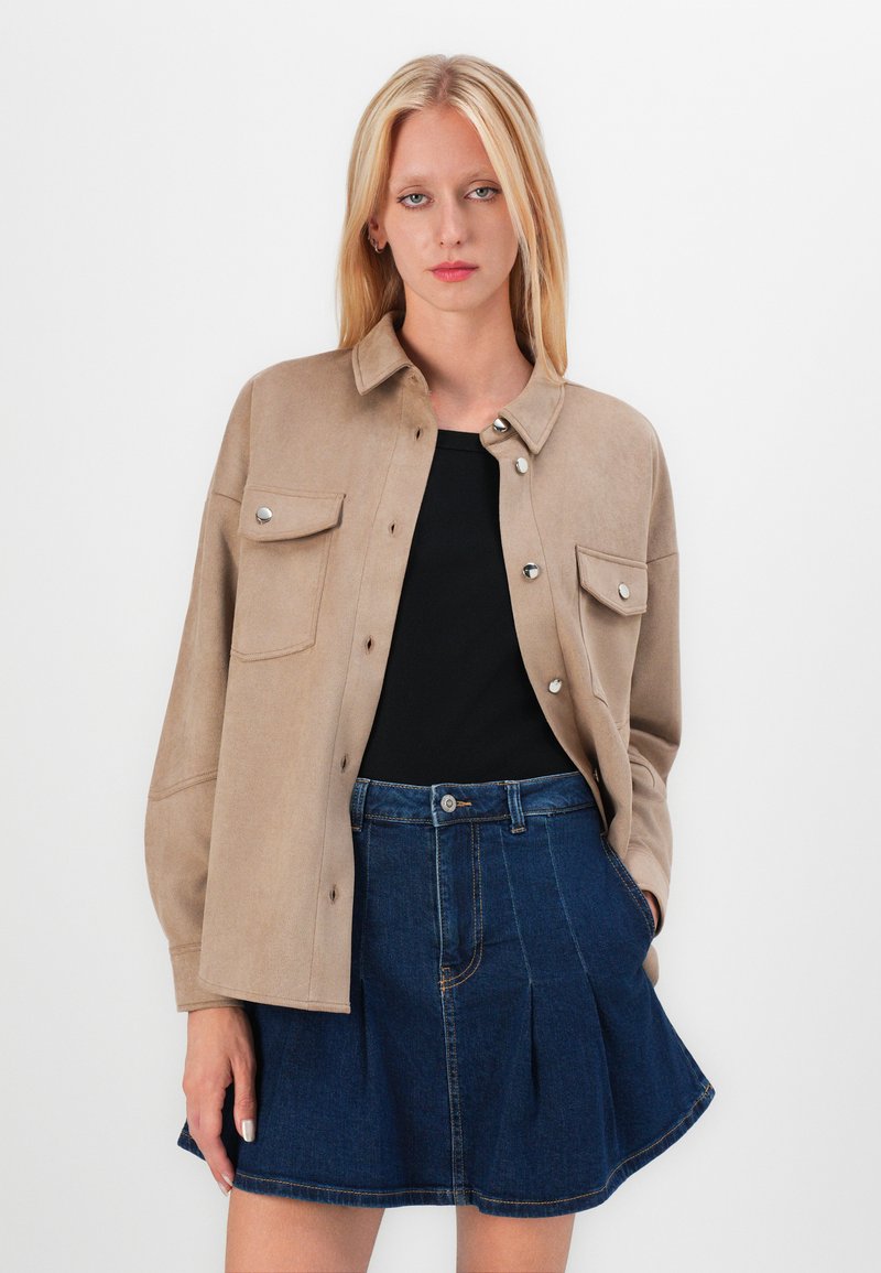 Giacca camicia in finta suede beige con bottoni a pressione argentati e due tasche sul petto, abbinata a una mini gonna di denim a trapezio.