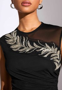 Black top featuring a sheer panel and embellished silver leaf design. Gathered texture on the body, round neckline, and short sleeves.