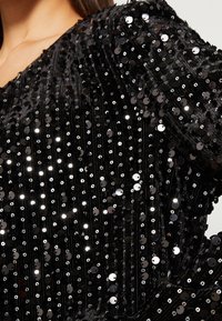 Svart paljettyg med vertikala ränder, prydd med skimrande, reflekterande paljetter som är arrangerade i ett tätt mönster över en texturerad yta.