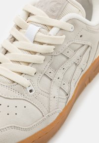 Sneaker beige in suede con lacci crema, dotata di una linguetta in rete, suola in gomma e un design testurizzato sui lati.