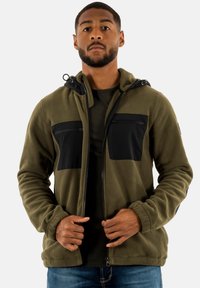 Olivgrüne Fleecejacke mit schwarzen Reißverschluss-Brusttaschen, verstellbarer Kapuze und glatter Textur. Verfügt über einen durchgehenden Reißverschluss und elastische Bündchen.