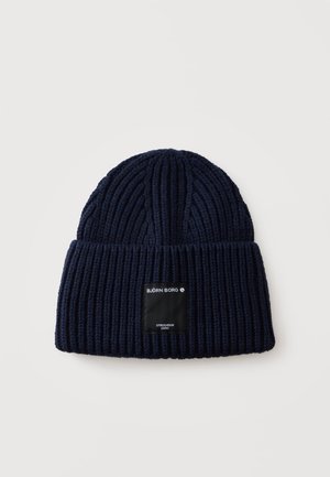 Bonnet en tricot côtelé bleu marine avec revers et étiquette rectangulaire noire portant la mention "BJÖRN BORG STOCKHOLM 1956" sur le devant.