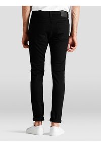 Černé slim-fit džíny s pěti kapsami, s poutkem na opasek a jemnými švy, kombinované s bílými teniskami.