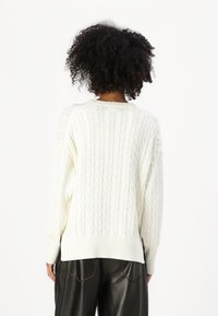 Maglione a maglia cable in bianco con una vestibilità rilassata, ampi polsini e orlo a costine, caratterizzato da una finitura testurizzata e design con spalle cadenti.