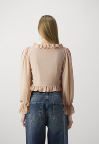 Dusty pink cropped blouse with ruffled neckline and cuffs, paired with high-waisted dark denim jeans featuring patch pockets.