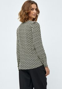 Schwarz-weiße gemusterte Bluse mit langen Ärmeln, rundem Ausschnitt und strukturiertem Stoff. Die Rückseite zeigt ein figurbetontes Design mit dezenten Raffung.