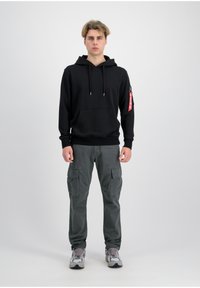 Black hooded sweatshirt with front pocket, grey cargo pants with multiple pockets, and grey and white sneakers. Zipper detail on the sleeve.
