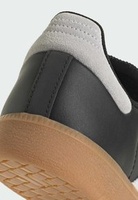 Tacco di scarpa in pelle nera con dettagli in suede grigio, suola in gomma testurizzata e cuciture bianche lungo la cucitura. Presenta una trama sul fondo per una migliore aderenza.