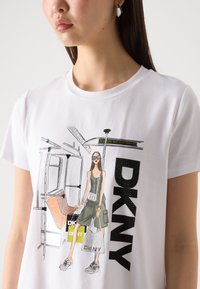 Balta medvilnės marškinėliai su grafine iliustracija, kurioje pavaizduota moteris su akinių nuo saulės, o priekyje yra spausdintas "DKNY" tekstas ir metro elementai.