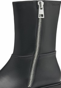 Black leather ankle boot with a metallic zip closure on the side, featuring a smooth texture and minimalistic design, with a stacked heel.