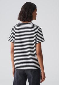 Black and white striped t-shirt with short sleeves and a crew neck, made of soft fabric, paired with dark denim jeans.