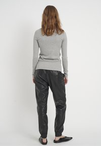 Graues, geripptes Langarmshirt und schwarze Lederjogginghosen mit elastischen Bündchen, kombiniert mit flachen schwarzen Schuhen, von hinten gezeigt.