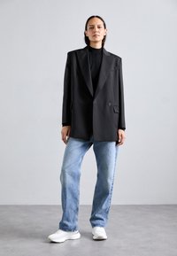 Czarna, oversize marynarka z wyraźnymi ramionami, zestawiona z jasnoniebieskimi dżinsami. Białe sneakersy dopełniają casualowy look.