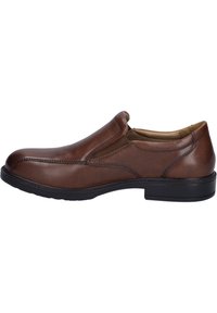 Brauner Leder-Schlüpfschuh mit runder Zehenform, elastischen Seitenteilen und einer strukturierten schwarzen Gummisohle. Gepunktete Details entlang der Ränder.