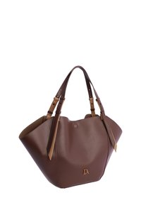 Bolso tote de cuero marrón con base ancha, dos correas de hombro ajustables y emblema dorado en el centro frontal.