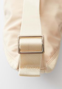 Borsa in tessuto beige con una texture lucida, dotata di una ampia tracolla crema e un dettaglio con fibbia in metallo dorato.
