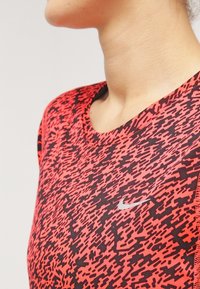 Punainen ja musta kuvioitu urheilupaita, jossa on pyöreä pääntie ja lyhyet hihat. Paidassa on pieni hopeinen Nike-logo rinnassa.