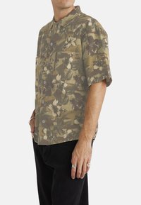 Short-sleeve shirt in olive green with floral pattern, featuring a collared neckline and two front pockets; made of lightweight fabric.