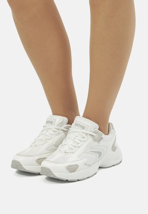 Zapatillas deportivas blancas con una parte superior texturizada, detalles en gris y una suela acolchada, que cuentan con cordones y un logotipo en la lengüeta.