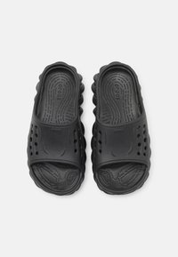 Černé nazouvací sandály s texturovanou gumovou podrážkou, obsahující ventilační otvory a zaoblený design. Výrazné logo na svrchní části.