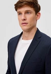 Granatowa marynarka wykonana z fakturowanej tkaniny, z jedną kieszenią na piersi i klapami w kształcie notcha, zestawiona z białym t-shirtem z okrągłym dekoltem pod spodem.