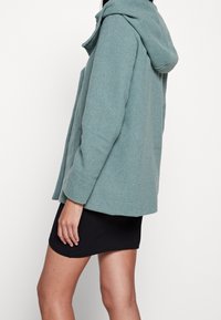 Teal wollen blend jas met kap, rechte snit en lange mouwen. Beschikt over een gestructureerde afwerking en een minimalistisch ontwerp.