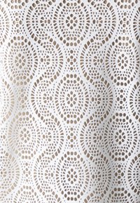 Hvit spettsduk med sirkulære mønstre i åpen hekledesign, som viser intrikate detaljer og en teksturert overflate.