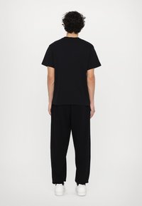 Sort bomulds t-shirt med korte ærmer, rund halsudskæring og afslappet pasform, sammen med matchende sorte sweatpants og hvide sneakers.
