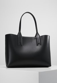 Czarna skórzana torba tote, gładka tekstura, prostokątny kształt, podwójne płaskie uchwyty z ostrymi akcentami, minimalistyczny design, brak widocznego okucia.