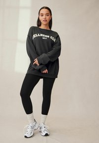 Must have suuruse, musta värvi sviiter, millel on valgete tähtedega "WELLNESS CLUB" tekst, koos mustade retuuside ja valgete spordijalatsitega, millel on hallid detailid.