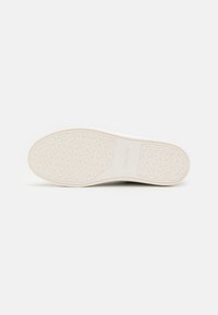 Semelle de chaussure en caoutchouc blanc cassé avec motif antidérapant texturé et logo en relief. Forme élégante et arrondie avec un design minimaliste.