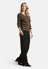 Black wide-leg pants paired with a textured, gold and black zigzag patterned sweater. The sweater features a V-neck and three-quarter sleeves.
