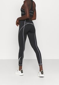 Czarny strój sportowy składający się z dopasowanej koszulki na ramiączkach z szarymi akcentami oraz legginsów z kontrastowymi szwami i bocznym logo. Połączony z białymi sneakerami.