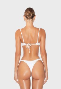 Set bikini bianco con top con lacci sul retro e parte inferiore con copertura minima. Texture liscia e lucida con un design semplice.