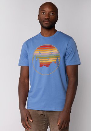 Blauw T-shirt met korte mouwen, voorzien van een cirkelvormige grafiek met horizontale strepen in geel, oranje en groen, waarop bomen en vogels zijn afgebeeld.