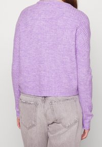 Lila gerippter Strickpullover mit Rundhalsausschnitt, cropped Design und langen Ärmeln, kombiniert mit hellgrauen Jeans.