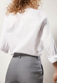 Biała koszula z długim rękawem o gładkiej fakturze, w połączeniu z szaro-czarnymi spodniami w kratę o wysokim stanie z bocznymi kieszeniami.