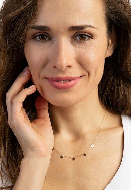 Gold necklace with small circular pendants, fine chain design, worn on a model. The background is neutral, highlighting the jewelry.