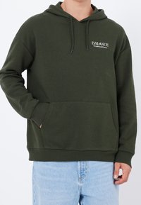 Felpa con cappuccio verde oliva con tasca a marsupio frontale, cappuccio con coulisse e logo con testo bianco. Realizzata in tessuto morbido e strutturato, con polsini a costine.