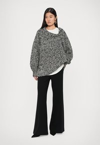 Oversized black-and-white knitted sweater with a textured pattern and wide sleeves, paired with high-waisted black trousers.