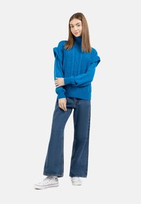 Pulover bleu tricotat cu guler înalt și modele texturate, asortat cu blugi cu croi larg și adidași albi.