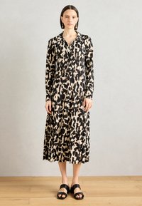 Abito a maniche lunghe in stampa animale nera e beige, con colletto e chiusura a bottoni. Abbinato a sandali neri a fascia.