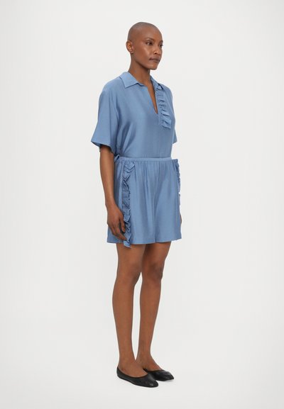 Short-sleeve blue dress with a collar, featuring a deep V-neck and ruffled accents on the sides, paired with black flats.