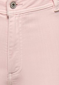 Približan pogled na svetlo rožnato jeansa tkanino, ki prikazuje kovinski gumb, zanko za pas in šive na sprednjem žepu.