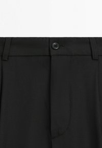 Black dress pants waist with button closure, belt loops, and fly seam detail on a white background.