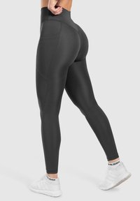 Leggings neri a vita alta realizzati in un tessuto liscio e elasticizzato. Presentano una tasca laterale e un design sagomato per migliorare la vestibilità.